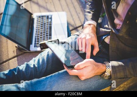 Cropped shot of young man using digital tablet et ordinateur portable sur trottoir Banque D'Images