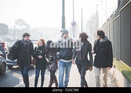 Six jeunes amis adultes bavarder tout en flânant le long de la rue de la ville Banque D'Images