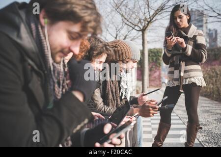 Six jeunes amis adultes en utilisant les smartphones et tablettes numériques dans park Banque D'Images