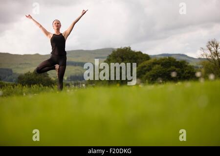 Mature Woman practicing yoga posture de l'arbre dans le champ Banque D'Images