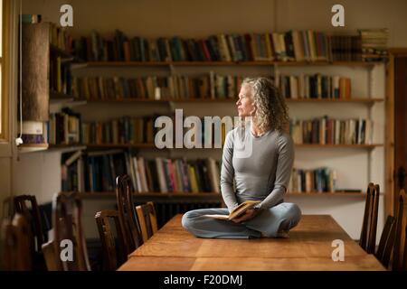 Mature Woman sitting cross legged sur table de cuisine à la fenêtre de Banque D'Images