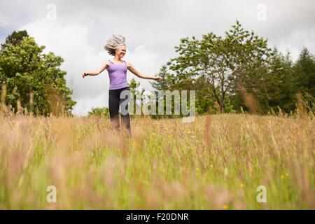 Femme mature avec de longs cheveux gris running through field Banque D'Images