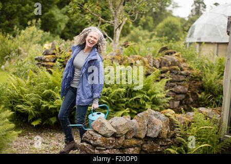 Portrait of young woman watering can in garden Banque D'Images