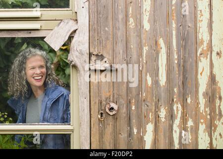 Smiling mature woman looking out window de serre Banque D'Images