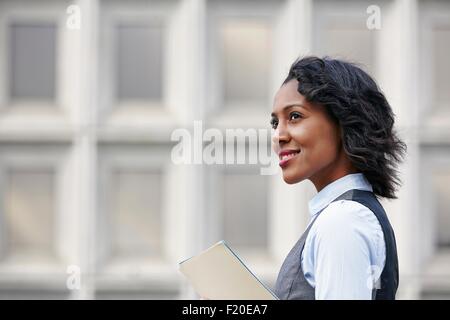 Portrait of young woman holding paper travail, à l'écart, smiling, portrait Banque D'Images