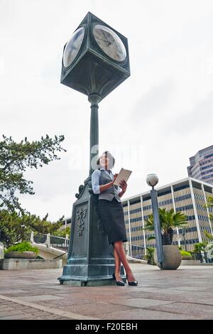 Young business woman leaning against réveil using digital tablet, looking away Banque D'Images