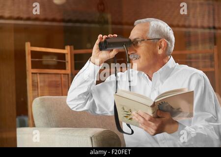 Senior man at home, l'observation des oiseaux par la fenêtre, à l'aide de jumelles Banque D'Images