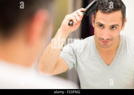 Mid adult man, à la recherche dans le miroir, se brosser les cheveux Banque D'Images