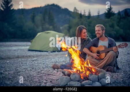 Jeune couple assis par camp à jouer de la guitare Banque D'Images