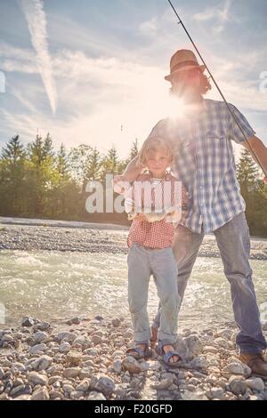 Mid adult man and boy à côté du fleuve montrant outre de poissons, looking at camera Banque D'Images