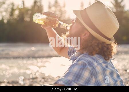 Vue latérale du Mid adult man wearing hat boire de la bière à partir de la bouteille de bière Banque D'Images