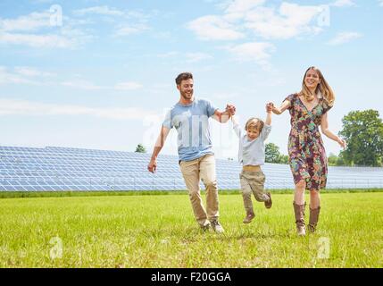 Mère et père tenant la main avec des fils, de marcher à travers champ en regard de la ferme solaire Banque D'Images