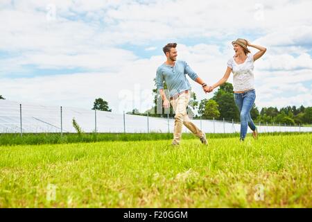 Young couple holding hands, courant à travers champs, à côté de la ferme solaire Banque D'Images