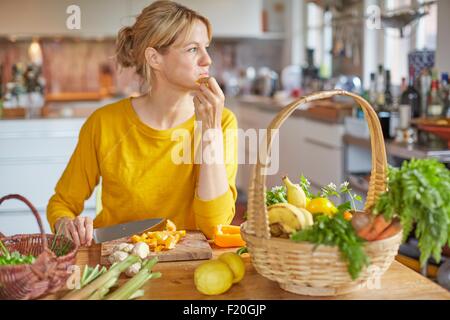 Mature Woman sitting at table de cuisine, hacher les légumes Banque D'Images