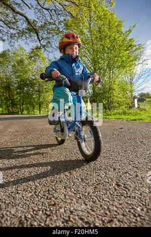 Boy wearing red casque de vélo cycling on rural road Banque D'Images