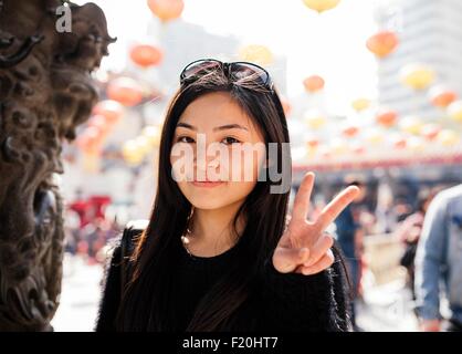 Portrait de jeune femme avec de longs cheveux et des lunettes sur la tête faisant signe de paix, looking at camera Banque D'Images