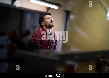 Jeune homme weaver à la recherche de vieux filets à machine à tisser dans l'usine de textile Banque D'Images