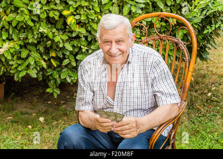 L'octogénaire ancien à chemise à carreaux est heureux tandis que les cartes à jouer dans le jardin de sa maison dans la campagne italienne Banque D'Images