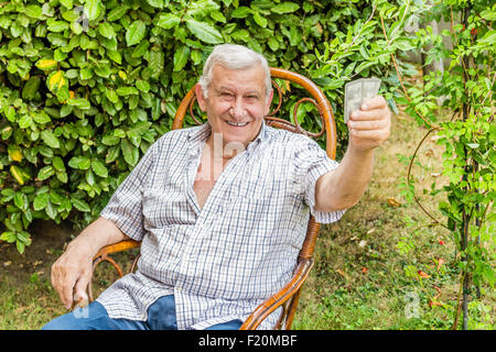 L'octogénaire ancien à chemise à carreaux est heureux tandis que les cartes à jouer dans le jardin de sa maison dans la campagne italienne Banque D'Images