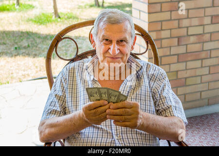 L'octogénaire ancien à chemise à carreaux est heureux tout en jouant aux cartes sur le patio de sa maison dans la campagne italienne Banque D'Images