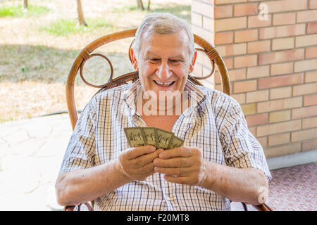 L'octogénaire ancien à chemise à carreaux est heureux tout en jouant aux cartes sur le patio de sa maison dans la campagne italienne Banque D'Images