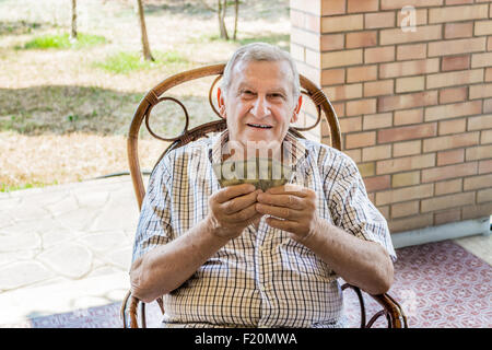 L'octogénaire ancien à chemise à carreaux est heureux tout en jouant aux cartes sur le patio de sa maison dans la campagne italienne Banque D'Images