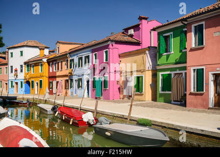 Italie, Vénétie, Burano, l'île de rangs colorés façades avec des bateaux sur un petit canal au premier plan. Banque D'Images