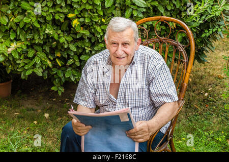 Retraite paisible, vieil homme lit le journal dans le jardin Banque D'Images