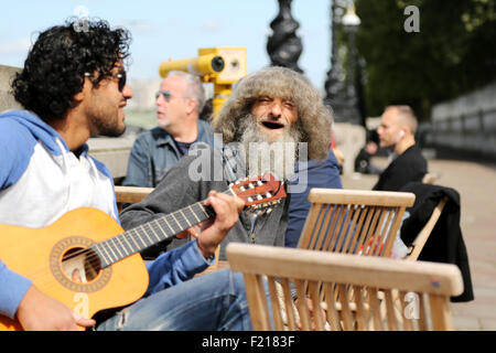 Un musicien ambulant jouant une guitare acoustique divertit les clients en dehors d'un décrochage à emporter café sur Southbank London un dimanche matin. Un gars excentrique. Banque D'Images