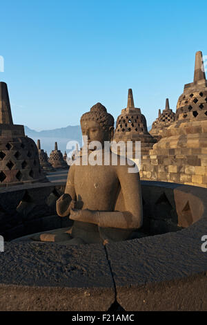 L'Indonésie, de Java, Borobudur, Bouddha assis sur le niveau supérieur allumé au début de la matinée, soleil chaud, entouré de stupas Banque D'Images