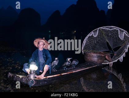 Pêcheur sur la rivière Li cormoran dans la nuit avec un filet blanc circulaire et ses oiseaux pour la récupération des poissons, Yangshuo, Chine, Asie Banque D'Images