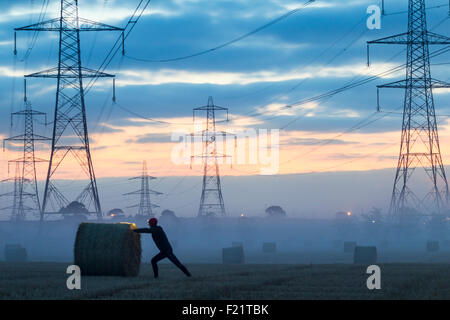 Pylônes électriques/lignes électriques National Grid dans la campagne britannique au lever du soleil. Jogging s'étirant au premier plan Banque D'Images