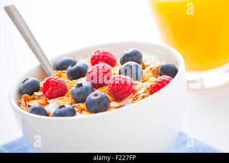 Un petit-déjeuner sain avec du muesli, fruits frais et jus d'orange. Profondeur de champ, l'accent sur les baies et de muesli. Banque D'Images