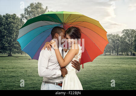 Moitié du corps d'un jeune couple doux sous un parapluie coloré dans un brouillard de pluie park Banque D'Images