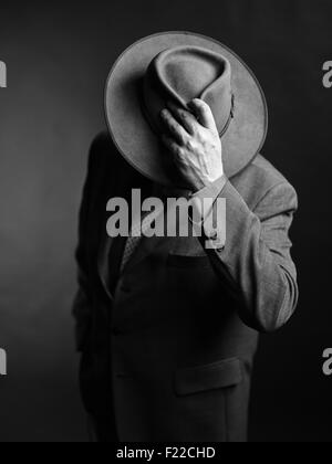 Homme portant costume sombre et il couvrant le visage avec un chapeau, noir et blanc Banque D'Images