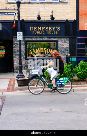 Un jeune homme à cheval sa bicyclette passé Dempsey's Irish Pub au centre-ville de Fargo, Dakota du Nord Banque D'Images