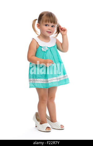Petite fillette de trois ans dans les chaussures de sa mère en studio sur un fond blanc. Banque D'Images