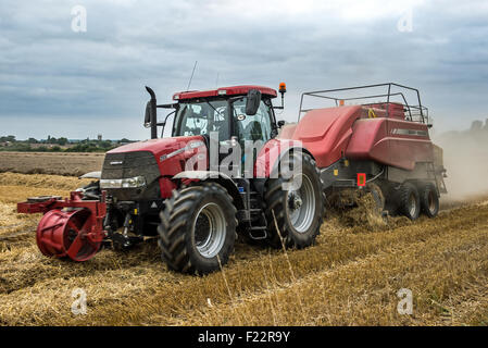 Un tracteur et écope en ramassant et tirer le faisceau de la forme du champ de blé. Banque D'Images