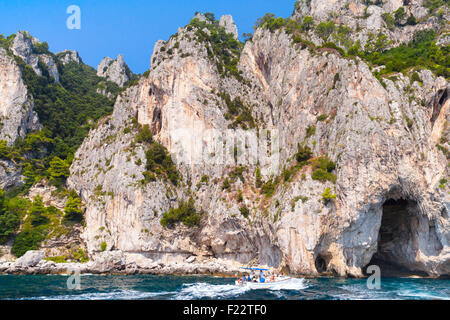 Les roches du littoral de l'île de Capri, petite embarcation à moteur avec les touristes aller près de la côte Banque D'Images