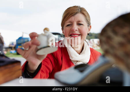 Une femme mature dans un manteau rouge tenant une figurine porcelaine vintage à un marché aux puces. Banque D'Images