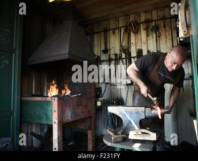 Blacksmith façonner un morceau de fer chaud sur une enclume dans une forge traditionnelle avec un feu ouvert. Banque D'Images