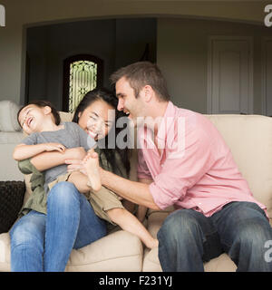 Une famille, un homme et une femme assis côte à côte sur un canapé à jouer avec leur jeune fils. Banque D'Images