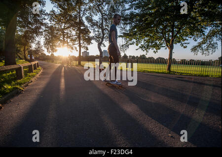 Un adolescent skateboards dans un parc de Londres au coucher du soleil Banque D'Images