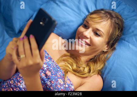 Young caucasian teenager de recevoir l'amour message de son nouveau petit ami. La jeune fille se pose sur lit et tient le téléphone contre son che Banque D'Images