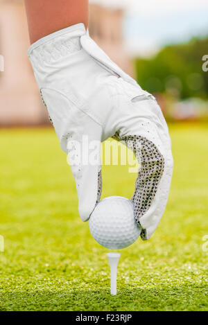 La main dans un gant blanc met la balle de golf sur un raccord en t Banque D'Images