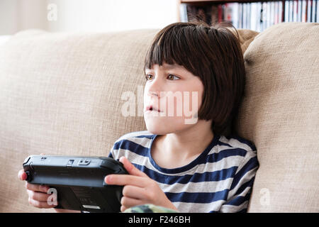 Homme caucasien enfant, garçon, 10-12 ans, assis tenant une console de jeu Nintendo Wii en concentrant les deux mains, la tête et épaules Vue de côté. Banque D'Images