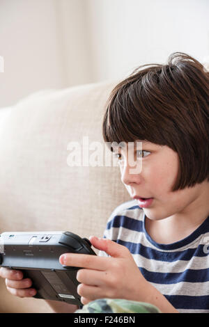 Homme caucasien enfant, garçon, 10-12 ans, assis tenant une console de jeu Nintendo Wii en concentrant les deux mains, la tête et épaules Vue de côté. Banque D'Images