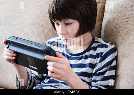 Homme caucasien enfant, garçon, 10-12 ans, assis tenant une console de jeu Nintendo Wii en concentrant les deux mains, la tête et épaules Vue de côté. Banque D'Images