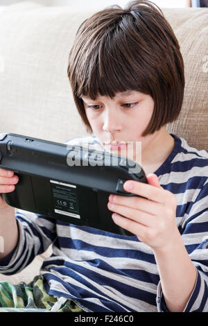 Homme caucasien enfant, garçon, 10-12 ans, assis tenant une console de jeu Nintendo Wii en concentrant les deux mains, la tête et épaules Vue de côté. Banque D'Images