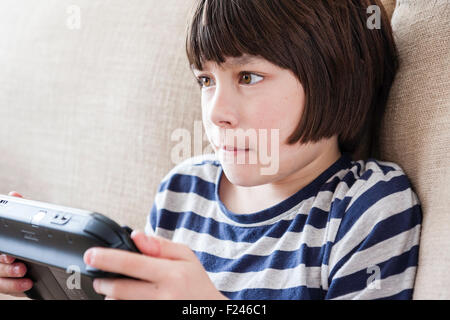 Homme caucasien enfant, garçon, 10-12 ans, assis tenant une console de jeu Nintendo Wii en concentrant les deux mains, la tête et épaules Vue de côté. Banque D'Images